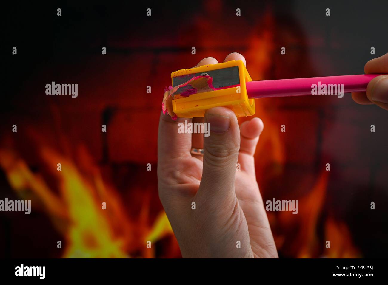 Eine Person schärft einen rosafarbenen Bleistift mit einem gelben Spitzer in der Nähe des Feuers. Stockfoto