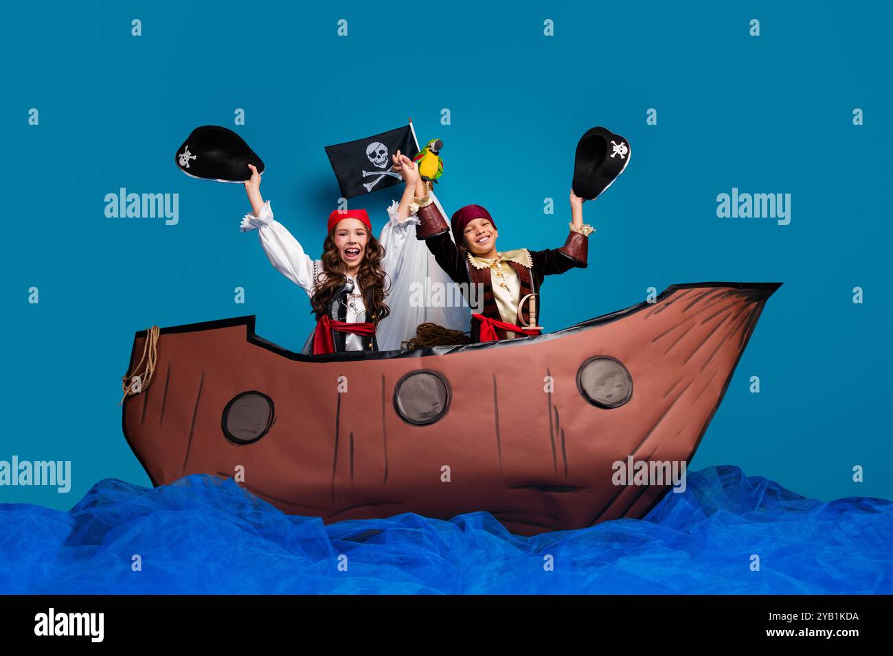 Foto in voller Größe von charmanten zwei kleinen Kindern heben Hüte feiern tragen Piraten halloween Kostüme Schiff Dekor isoliert auf blauem Hintergrund Stockfoto