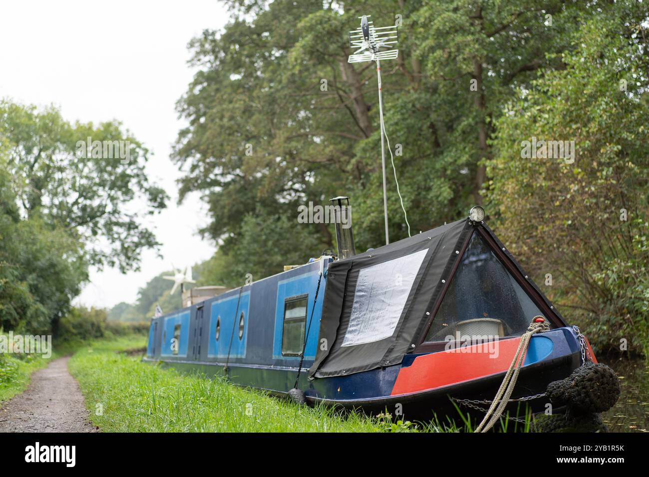 Vorderansicht eines Hauskanalbootes mit einem tv-Antennenmast an der Vorderseite des Bootes, der an der Seite eines britischen Kanals verankert ist. Stockfoto