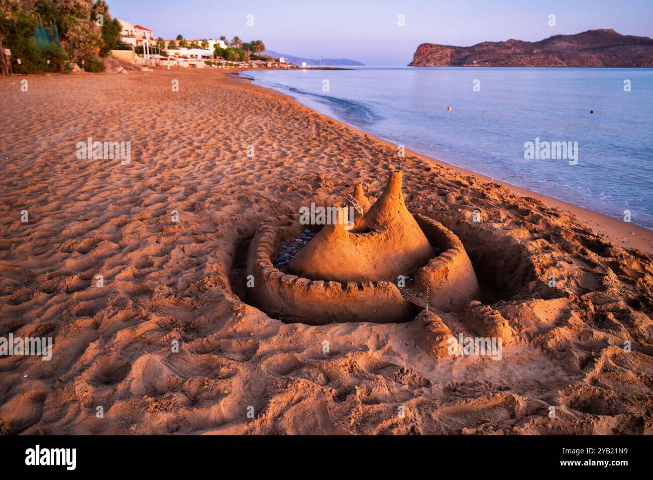 Kleine Sandburg am leeren Strand bei Sonnenaufgang mit schöner warmer Beleuchtung. Gegend von Kato Stalos, Teil der Insel St. Theodora, Kreta, Griechenland. Stockfoto