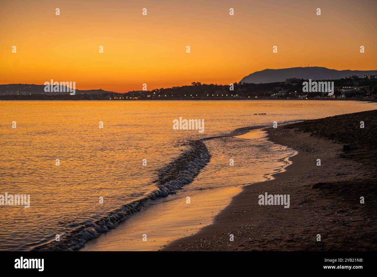 Fantastischer orangener Sonnenaufgang über dunklem Strand, ruhiges Meer und Berge am Horizont. Kato Stalos, Kreta, Griechenland. Stockfoto