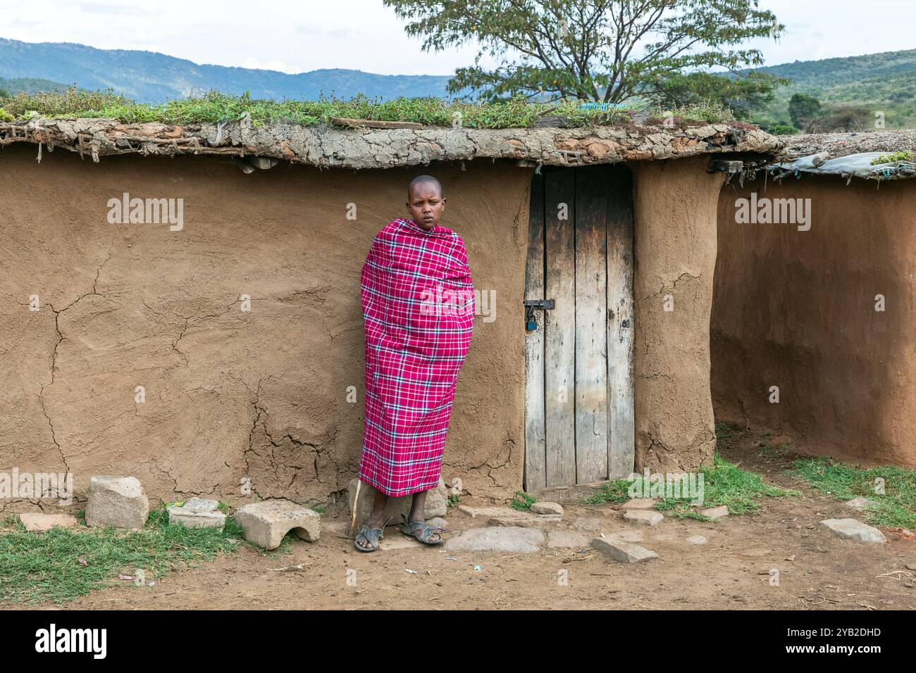 Junger Masai-Junge, der vor einem traditionellen Masai-Wohnhaus aus Kuhmist, Schlamm und Holzzweigen steht, Masai Mara, Kenia, Afrika Stockfoto