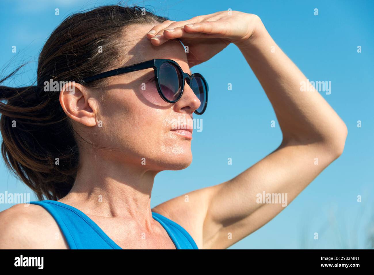 Frau, die ihr Gesicht mit der Hand vor der Sonne schützt Stockfoto