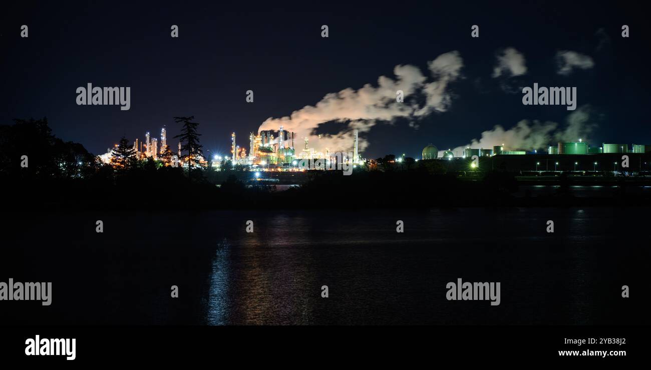 Dampf aus der industriellen Ölraffinerie driftet über dem dunklen Nachthimmel über dem beleuchteten Industriekomplex Stockfoto