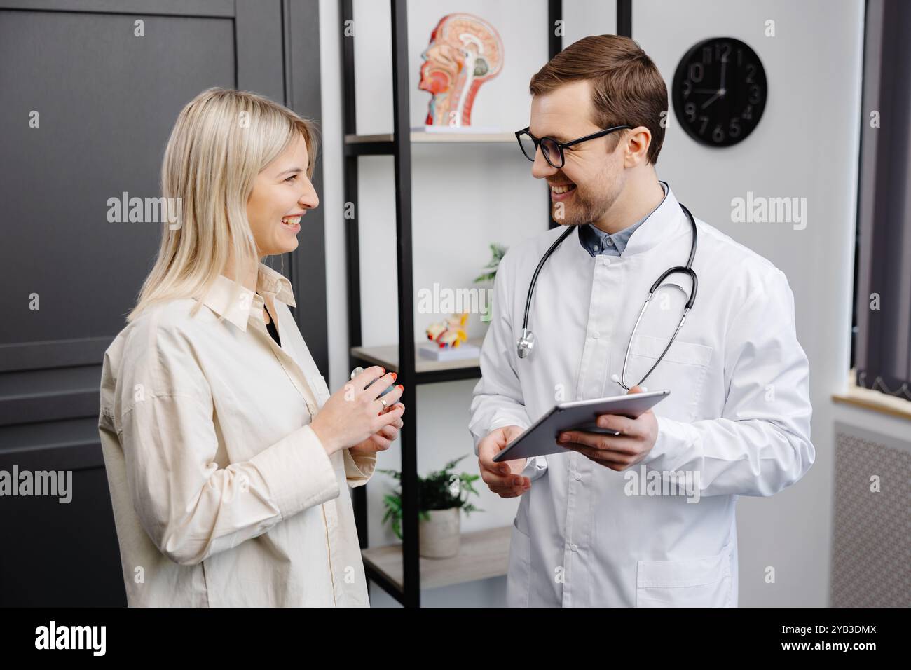 Männlicher Arzt, der einen Aerosolinhalator in der Hand hält, bei einer Demonstration einer Patientin in seiner Praxis. Stockfoto