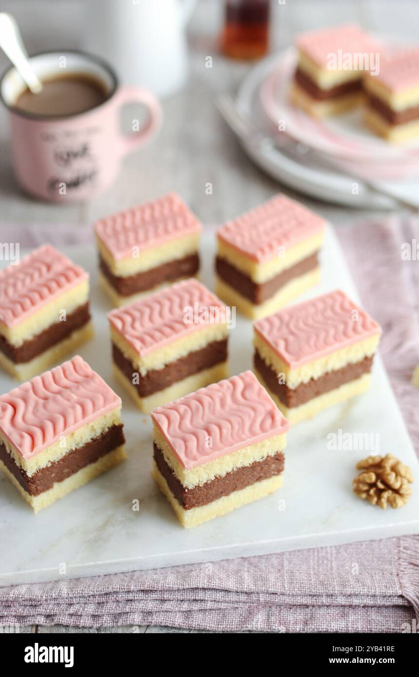 Rum-Punsch-Kuchen mit Rum und weichen Kuchenschichten mit rosafarbener Glasur. Eine Tasse Kaffee und eine Flasche Rum im Hintergrund. Stockfoto