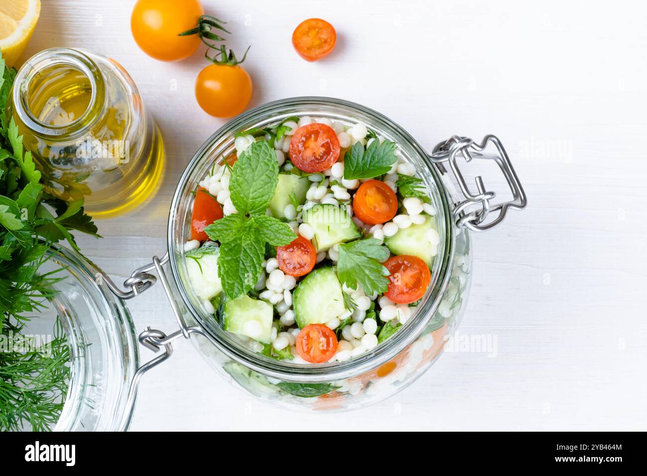 Frischer Couscous-Salat in einem Glas mit Gurken, Tomaten, Kräutern, Zitrone mit Zutaten auf weißem Hintergrund. Tabbouleh-Salat. Gesunder Vegetarier Stockfoto