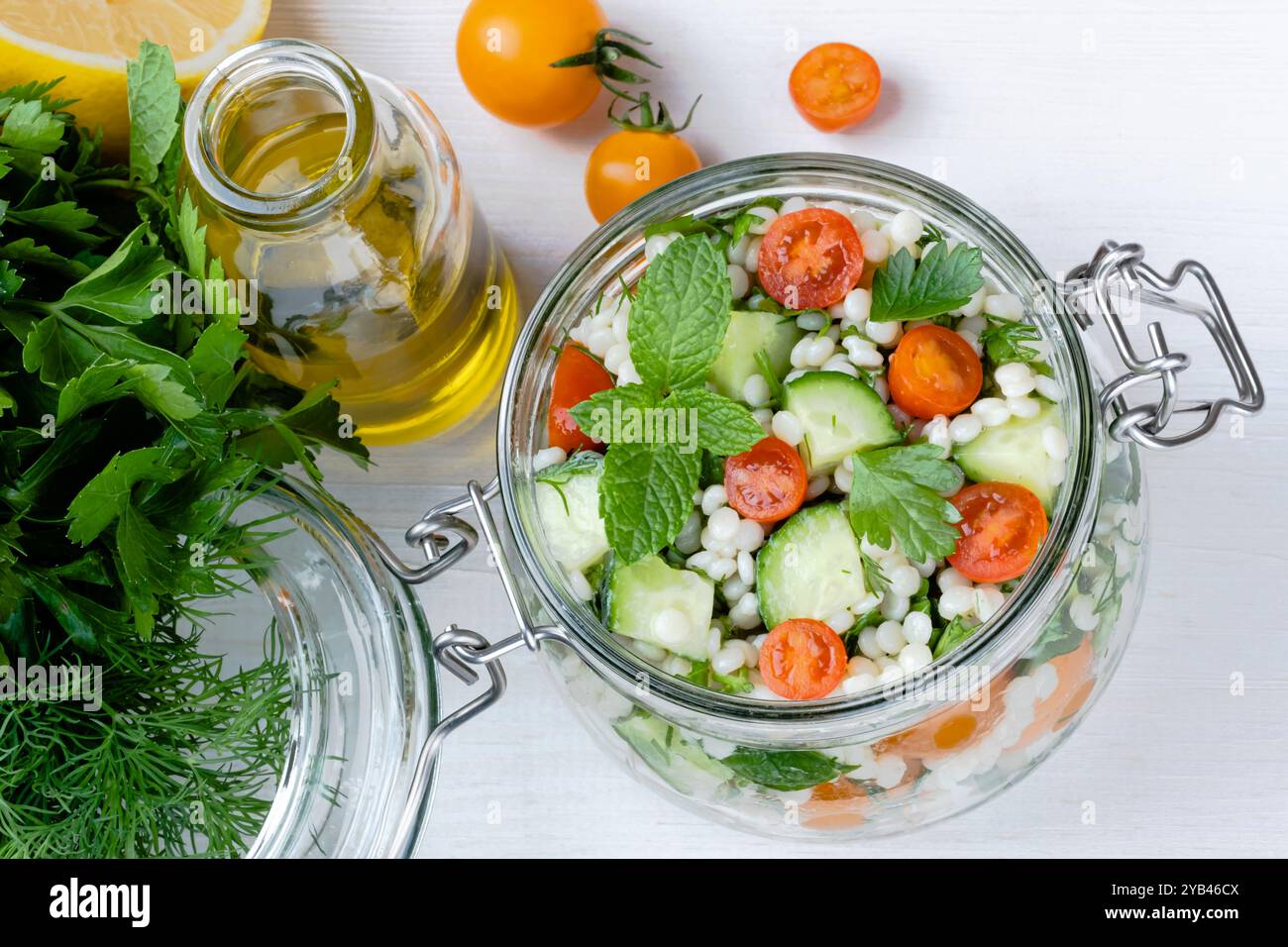 Frischer Couscous-Salat in einem Glas mit Gurken, Tomaten, Kräutern, Zitrone mit Zutaten auf weißem Hintergrund. Tabbouleh-Salat. Gesunder Vegetarier Stockfoto