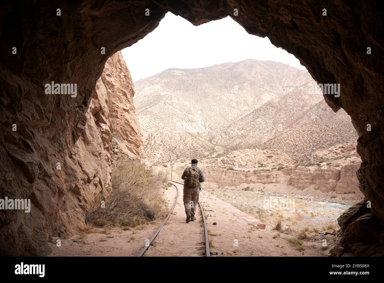 Ausgang eines Zugtunnels, draußen läuft eine Person entlang des Gleises. Im Hintergrund eine Berglandschaft. Konzepte: Das Licht am finden Stockfoto