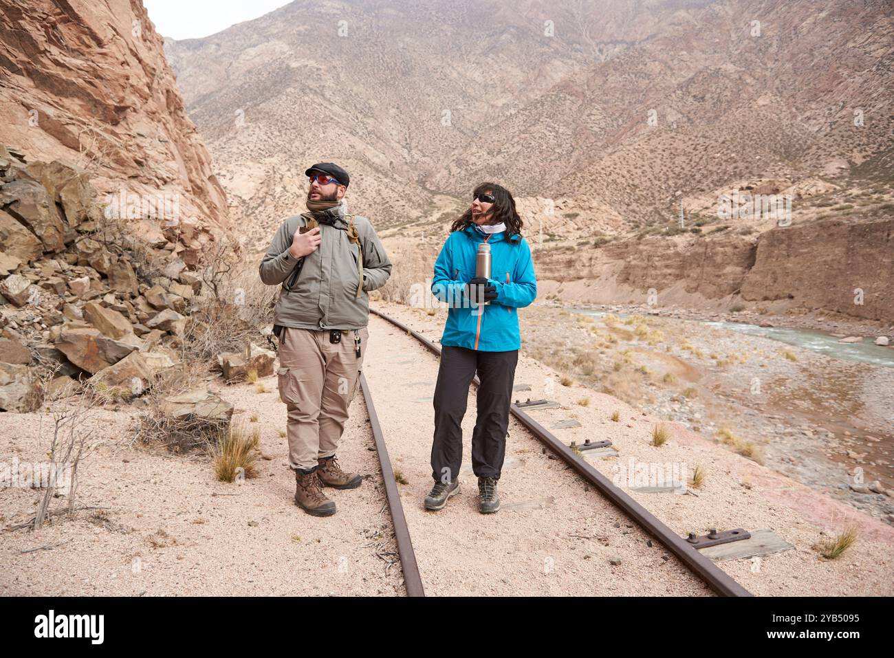 Ein paar Reisende Freunde, Mann und Frau, die die Gleise entlang laufen. Im Hintergrund befindet sich ein Tunnel. Beide schauen nach oben und sehen etwas an Stockfoto