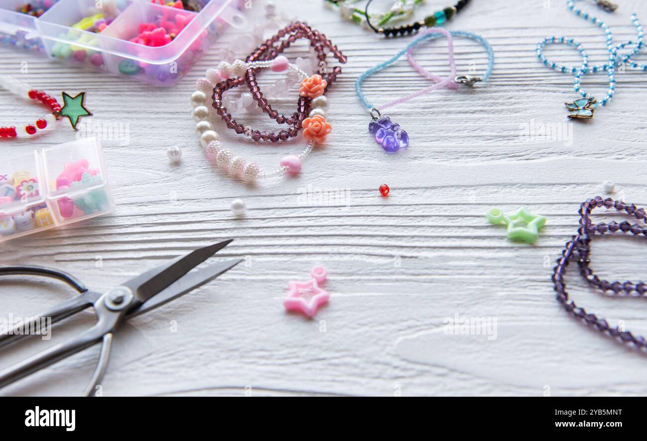 Verschiedene Perlen, Anhänger und Werkzeuge sind auf einem Holztisch verstreut, während ein Künstler einzigartige Schmuckstücke in einer lebendigen Bastelsession entwirft. Stockfoto