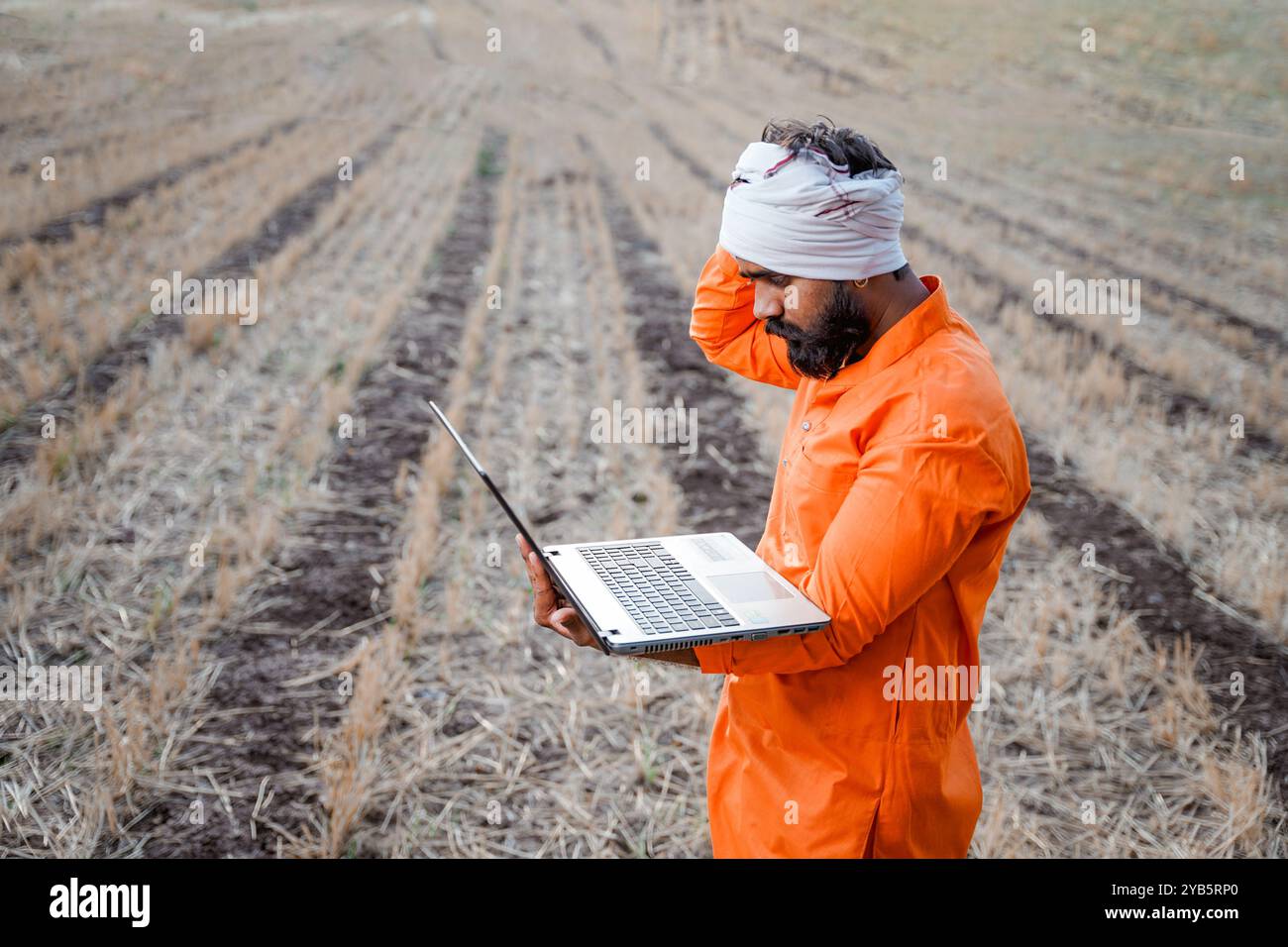 Indischer ländlicher Landwirt, der auf dem Feld der Feldfrüchte an einem Laptop arbeitet Stockfoto