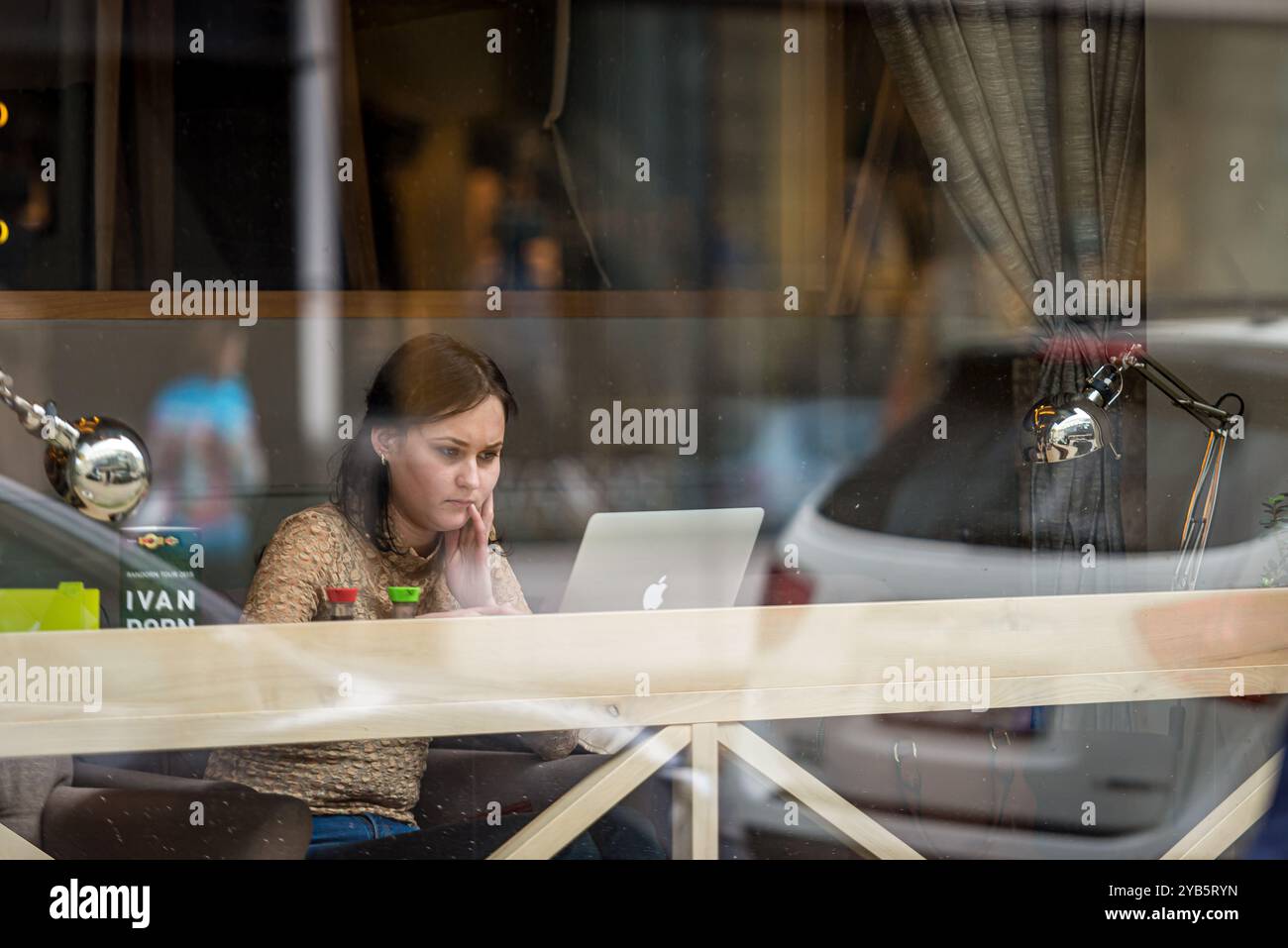 Riga, Lettland, 24. April 2015: Junge Frau arbeitet an einem Laptop in einem gemütlichen Café mit einer Glaswand in einem Stadtgebiet Stockfoto