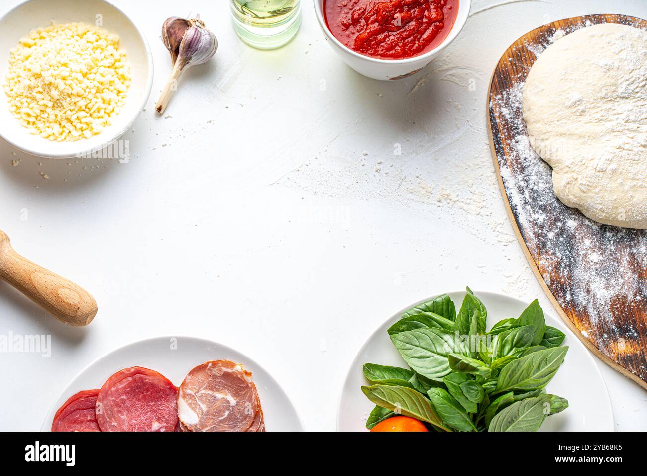 Zutaten für die Zubereitung italienischer Pizza: Teig, Tomatensauce, Parmesan, Tomaten, Basilikum, Knoblauch, Wurst auf einem weißen Tisch. Richtiges Pizzarezept. Kopierraum . Stockfoto
