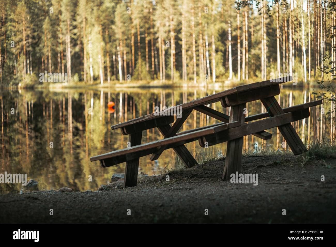 Holztisch, der allein am Ufer eines kleinen Sees sitzt. Spiel von Schatten und Licht, gemütliches Gefühl. Stockfoto