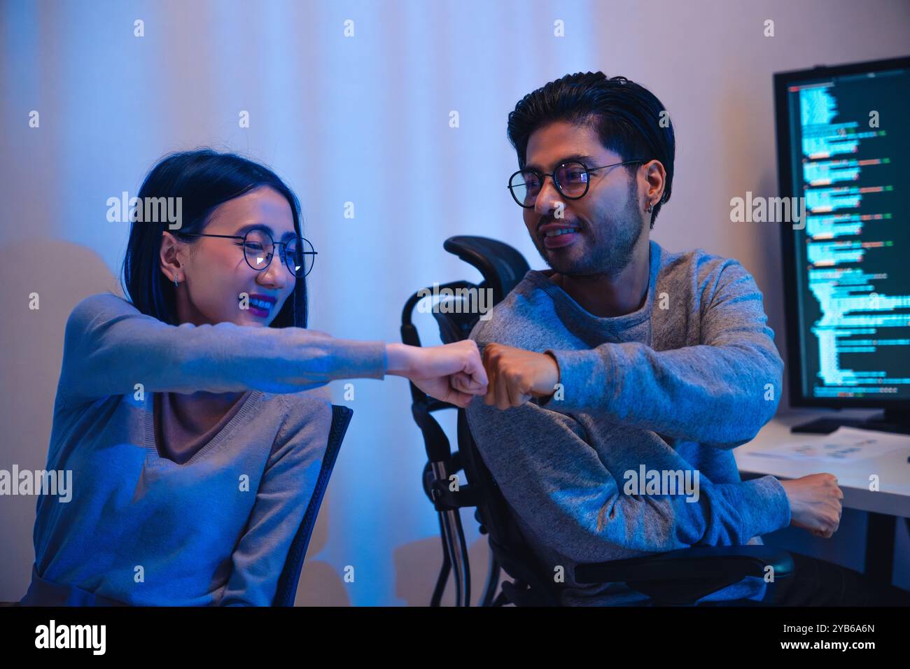 asiatische und indische Entwicklerteams klatschen sich für Projekterfolg mit Software-Computer in der Nacht im Büro Stockfoto