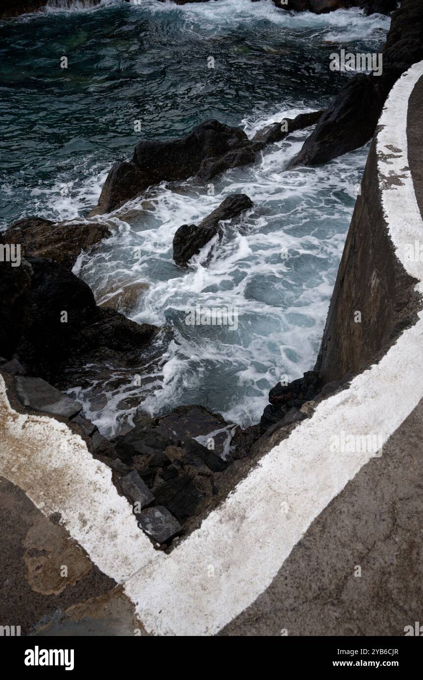 Wellen brechen an den natürlichen Pools von Porto Moniz unter einer scharfen Betonkante gegen vulkanische Felsen Stockfoto