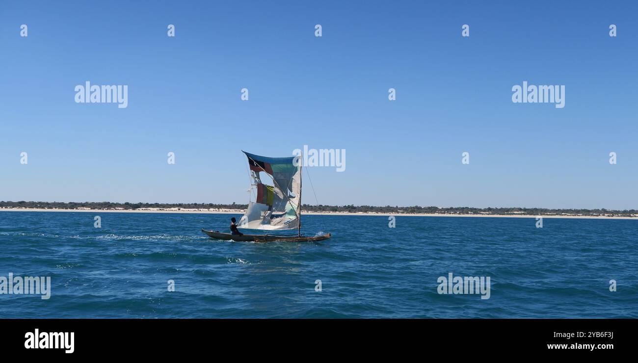 Kleines Pirogue-fischerboot mit aufgerissenem Segel, das am Morgen entlang der Küste des westlichen Madagaskars in der Nähe von Belo Sur Mer segelt. Stockfoto