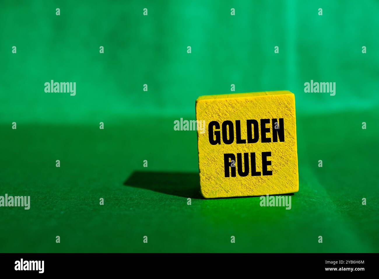 Goldene Regelbotschaft auf gelbem Holzwürfel mit grünem Hintergrund. Konzeptionelles goldenes Regelsymbol. Kopierbereich. Stockfoto