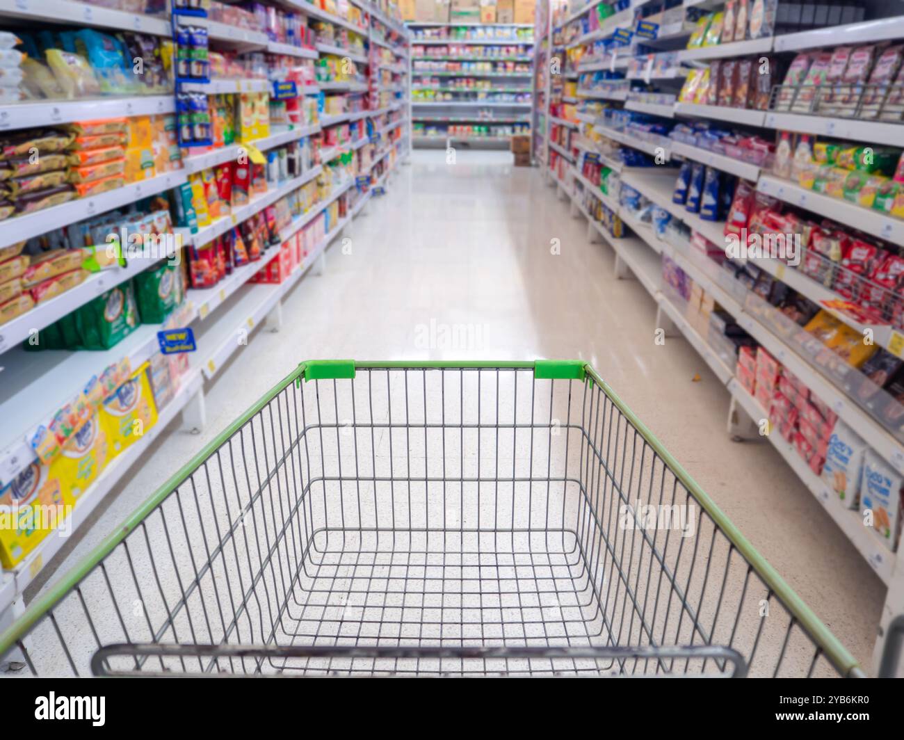 Leere rote Warenkorbansicht mit warmem Licht, Einkaufswagen im Supermarkt, Trolley im Kaufhaus abstrakte Unschärfe der bunten Regale. Stockfoto