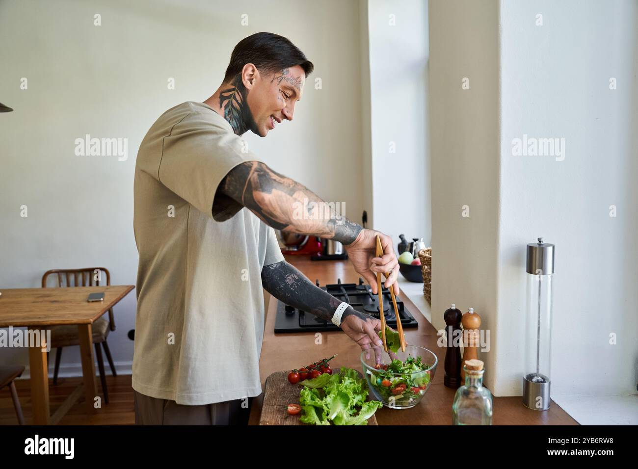 Ein junger, gutaussehender Mann mischt gekonnt Gemüse in einer Schüssel, während er zu Hause kocht. Stockfoto