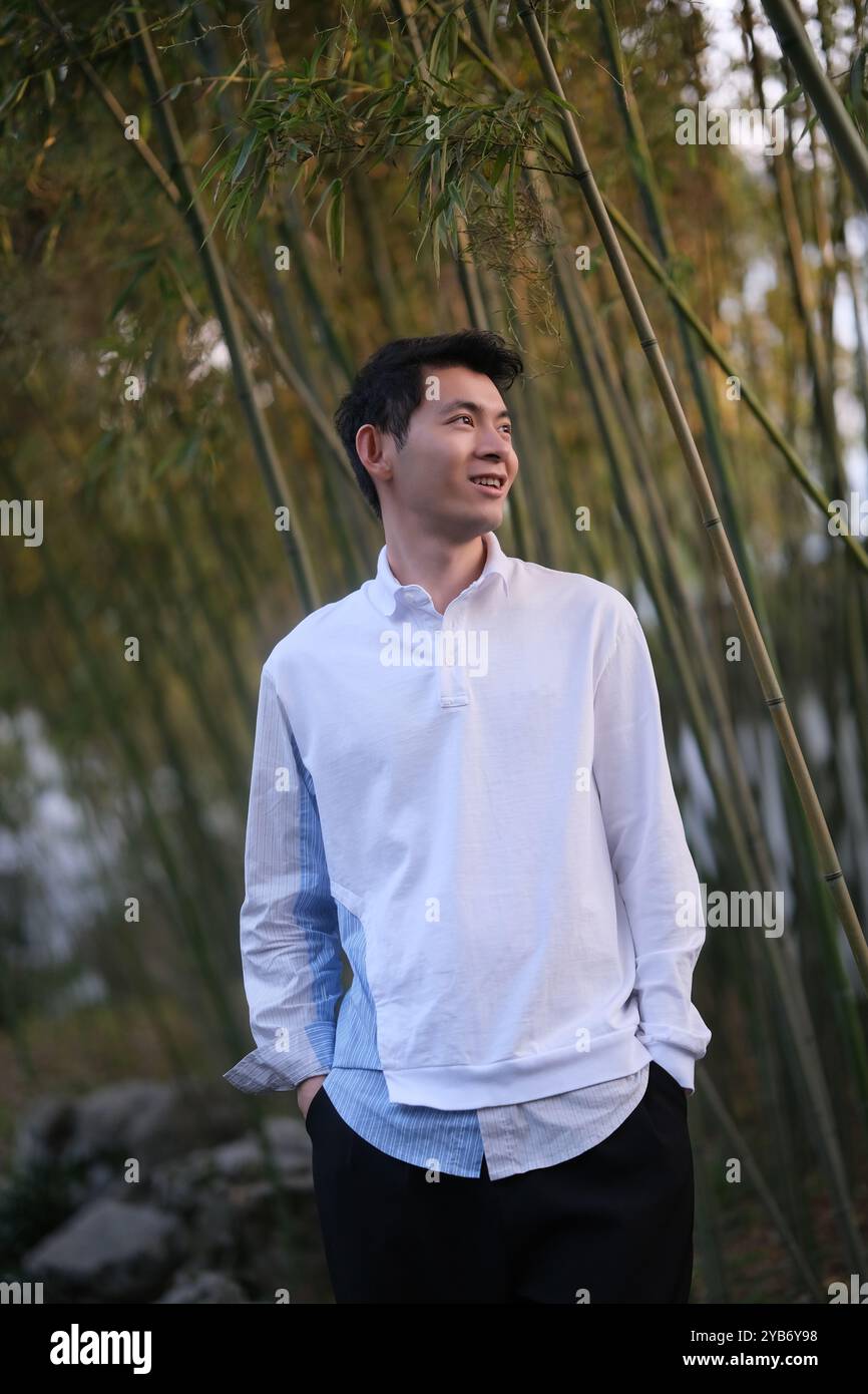 Lächeln Sie hübscher asiatischer junger Mann, Hände in Taschen, im Bambushain Stockfoto