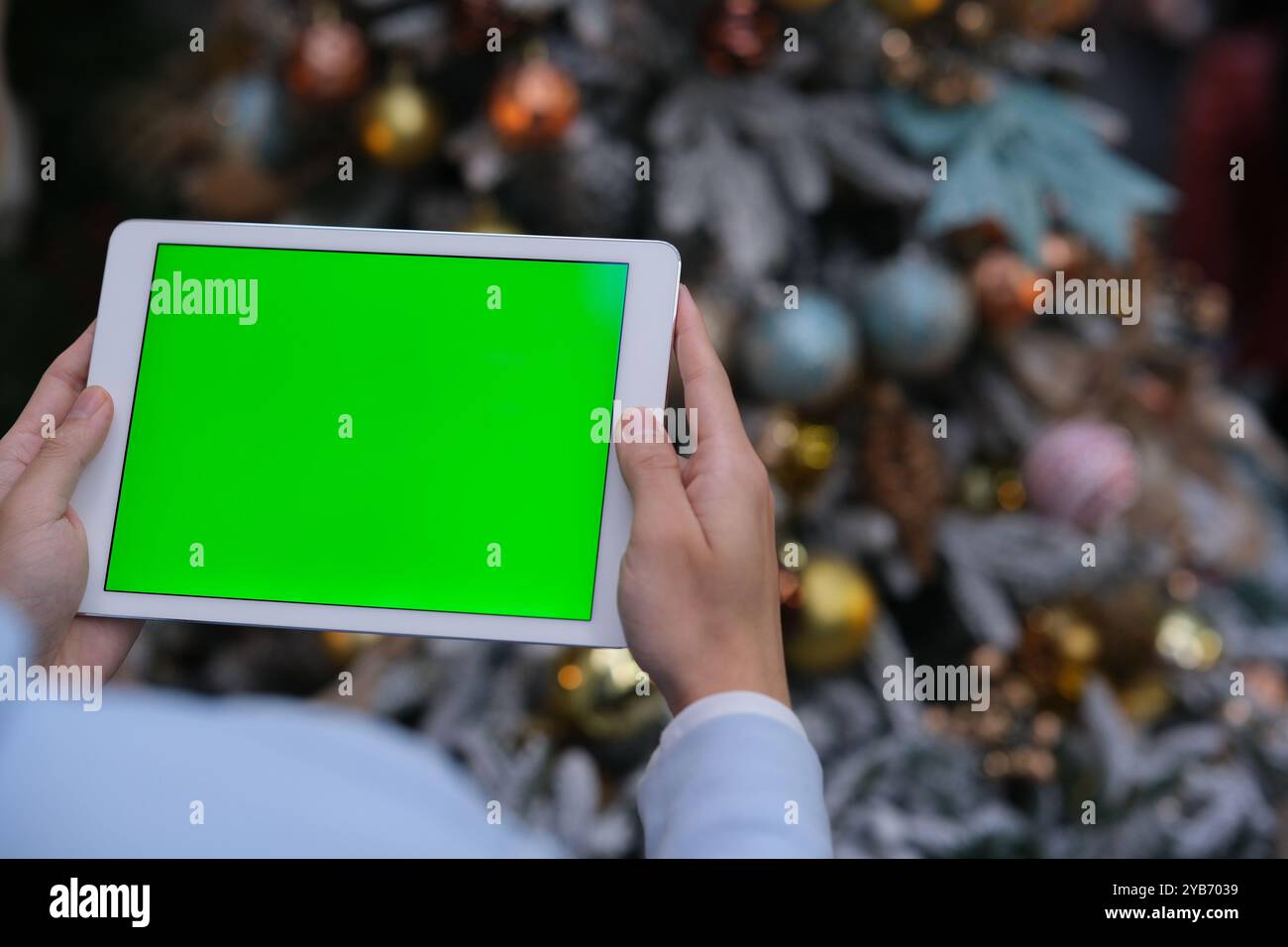 Hand hält den Tablet-Computer mit grünem Bildschirm zu Weihnachten. Über die Schulter Stockfoto
