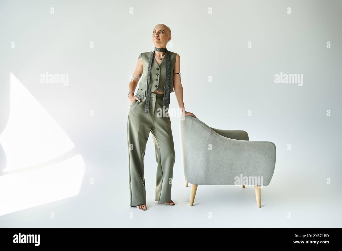 Eine junge kahlköpfige Frau steht selbstbewusst neben einem modernen Stuhl und zeigt ihre einzigartige Schönheit. Stockfoto