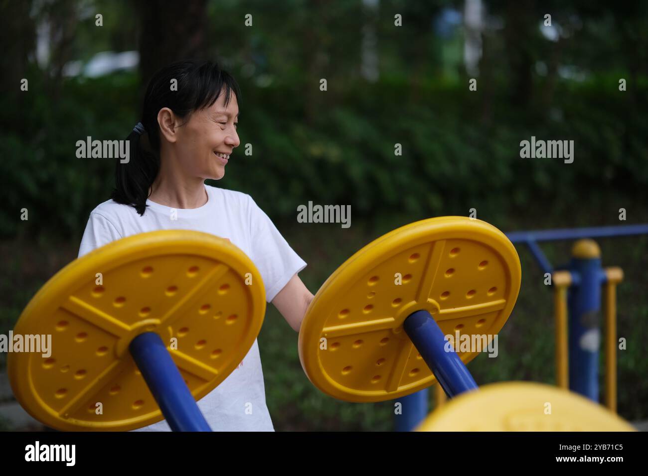 Eine lächelnde alte Chinesin trainiert auf Fitnessgeräten im Freien. Gesunder Lebensstil Stockfoto