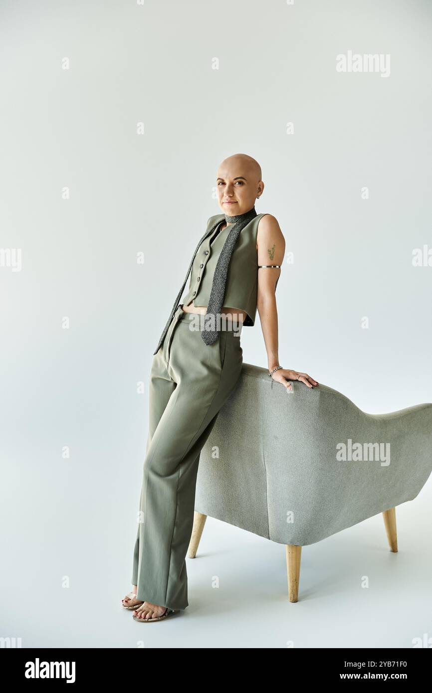 Eine junge kahlköpfige Frau mit Alopezie steht anmutig an einem modernen Stuhl und zeigt ihre Eleganz. Stockfoto