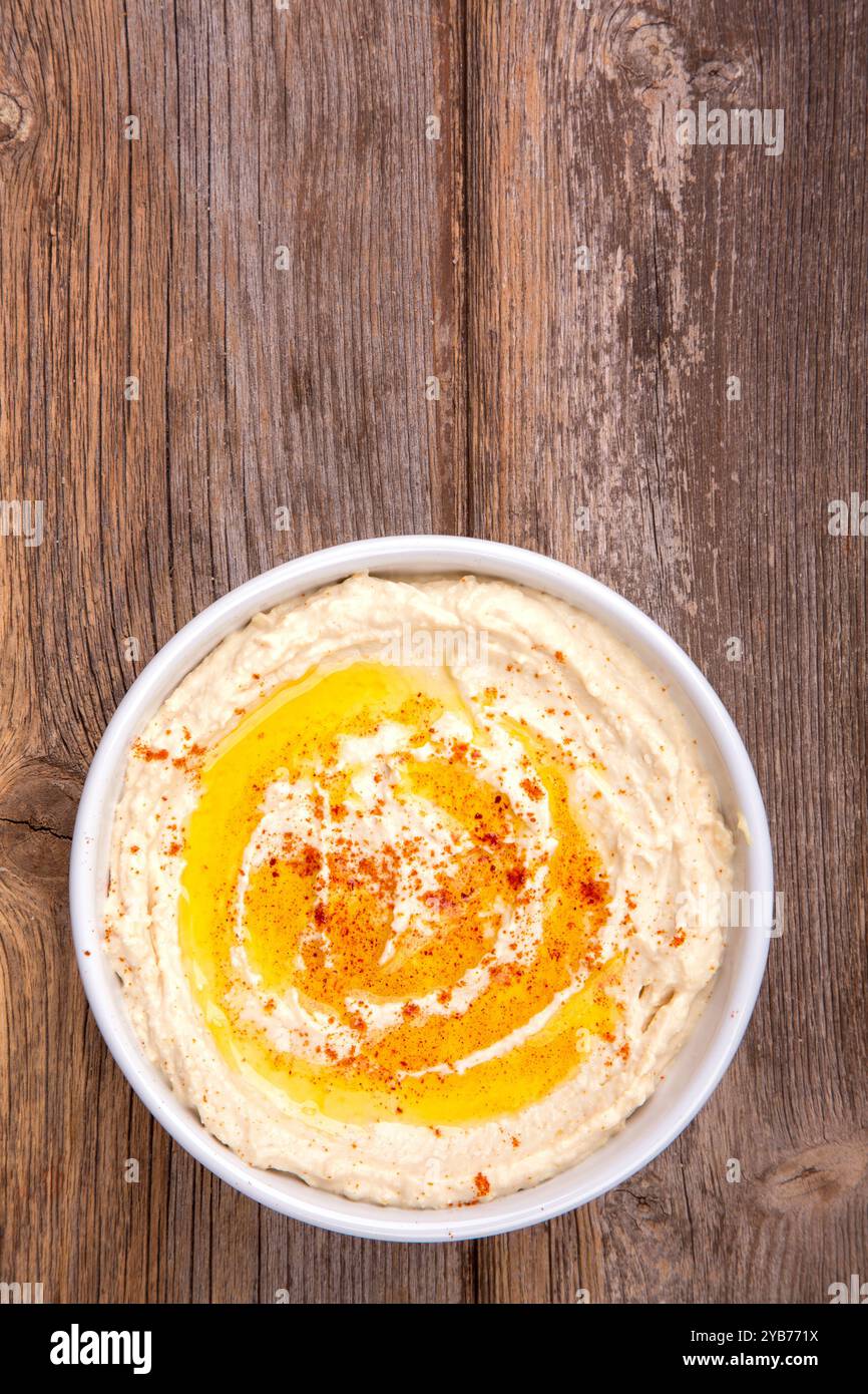 Eine Schüssel mit cremigem Hummus, mit Olivenöl getränkt und mit Paprika bestreut, über rustikalem Holzhintergrund. Leerzeichen für Text. Stockfoto