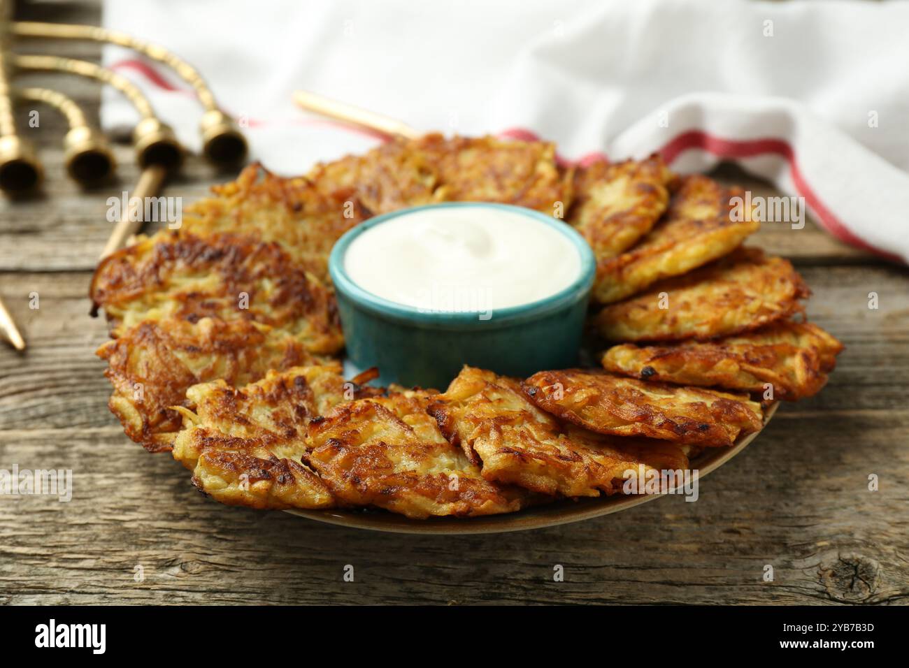 Leckere Kartoffelpfannkuchen, Sauerrahm, Menora und Kerzen auf Holztisch, Nahaufnahme. Hanukkah festliches Essen Stockfoto