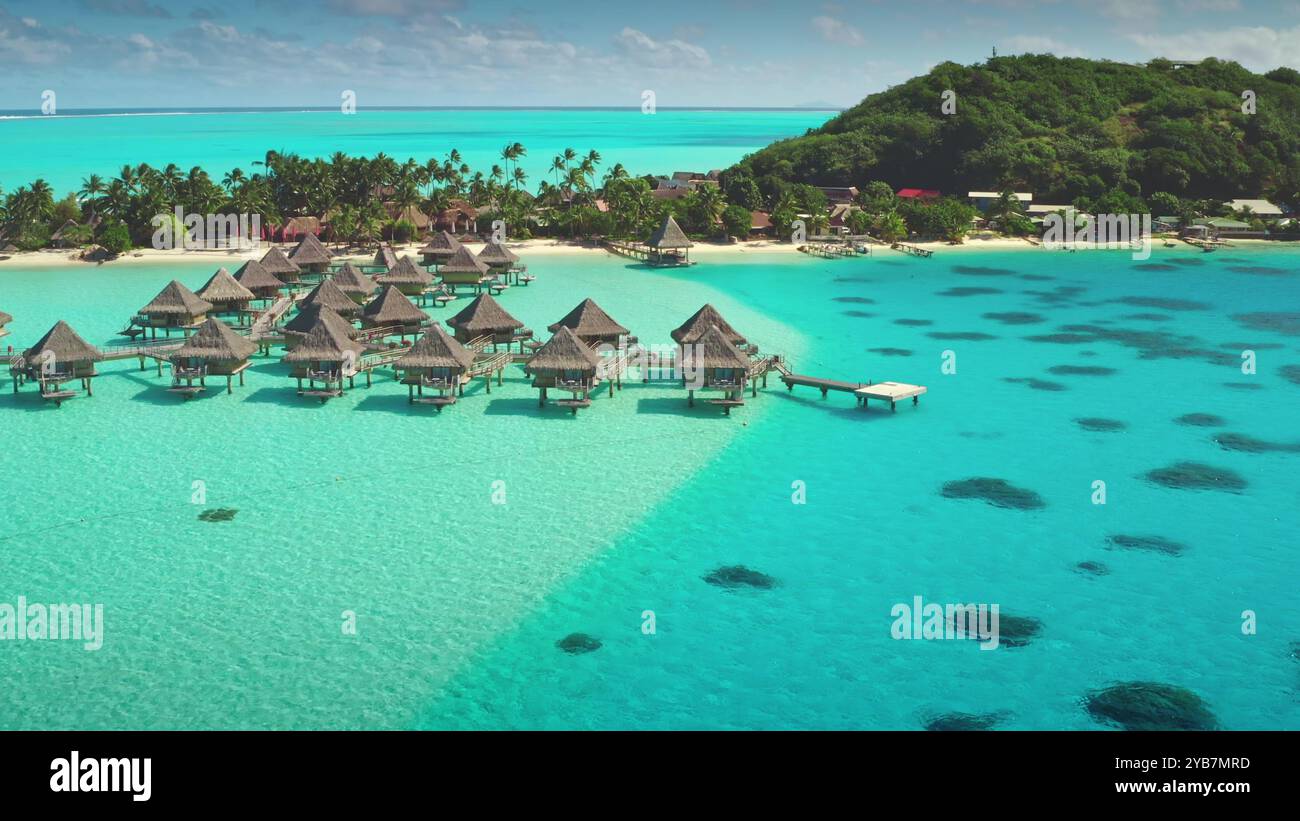 Luxuriöse Bungalows über dem Wasser in türkisfarbener, kristallklarer Lagune mit tropischem Inselsandstrand im Hintergrund. Blick auf die Drohne von einem perfekten exotischen Sommerurlaub. Wilde Natur Hintergrund Stockfoto