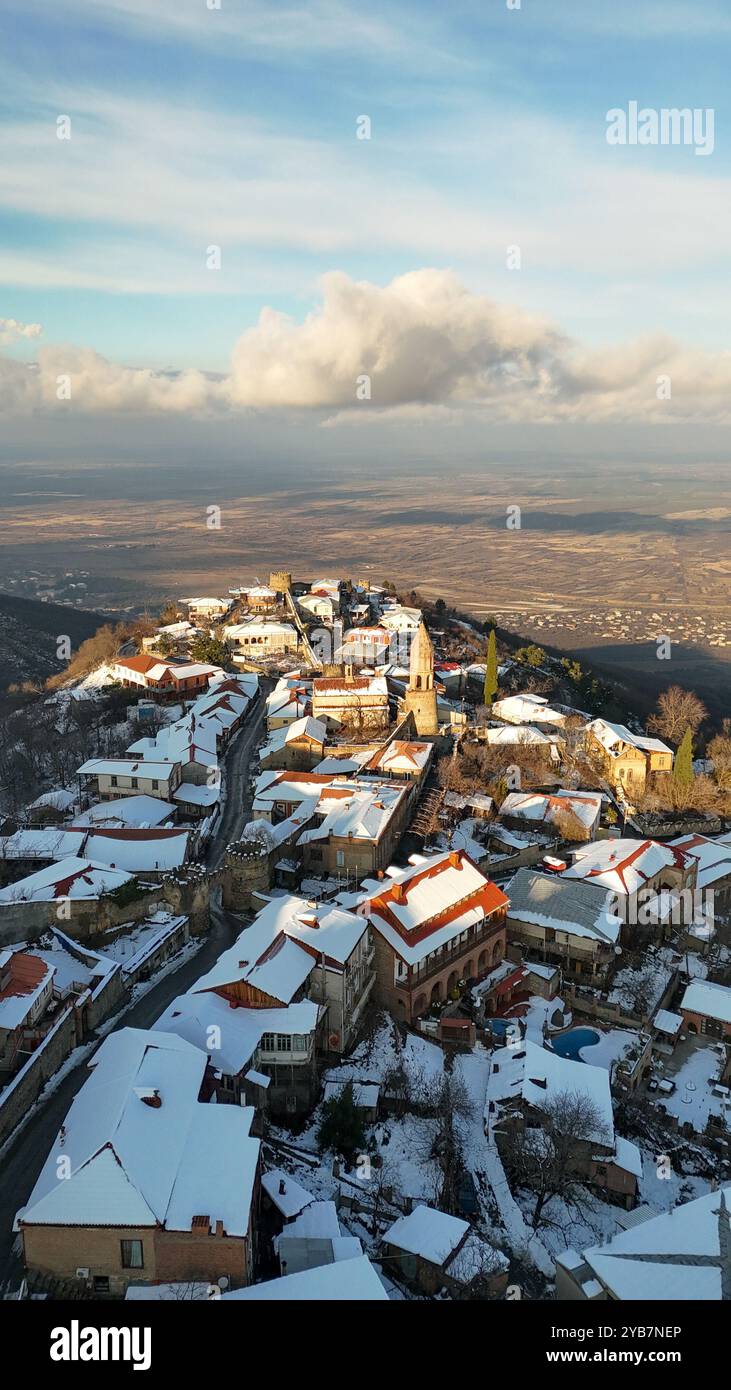 Ein atemberaubender Blick aus der Luft auf ein schneebedecktes Dorf auf einem Hügel in Georgia mit historischen Steinhäusern, Häusern mit roten Dächern und einem Kirchturm. Stockfoto