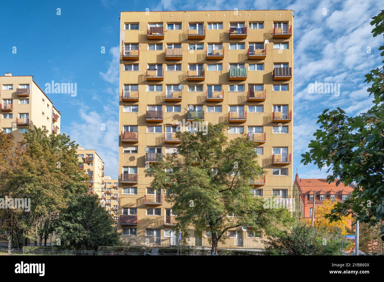 Ein modernes Apartmentgebäude mit mehreren Balkonen unter einem hellblauen Himmel. Umgeben von üppigem Grün, ist dieses Gebäude beispielhaft für urbanes Leben Stockfoto