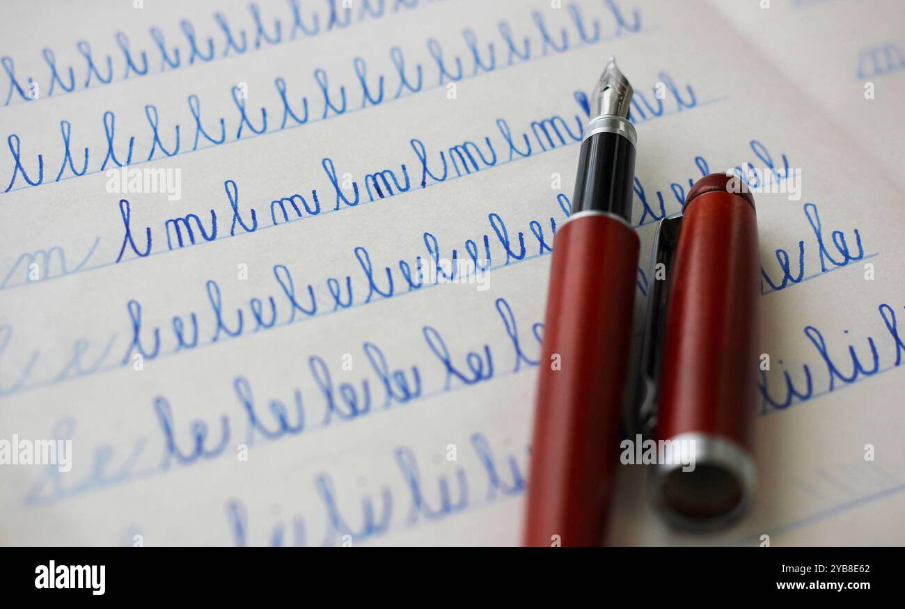 Nahaufnahme eines burgunderroten Füllfederschreibers und blauer Buchstaben, geschrieben von einem Kind in einem Notizbuch aus Papier Stockfoto