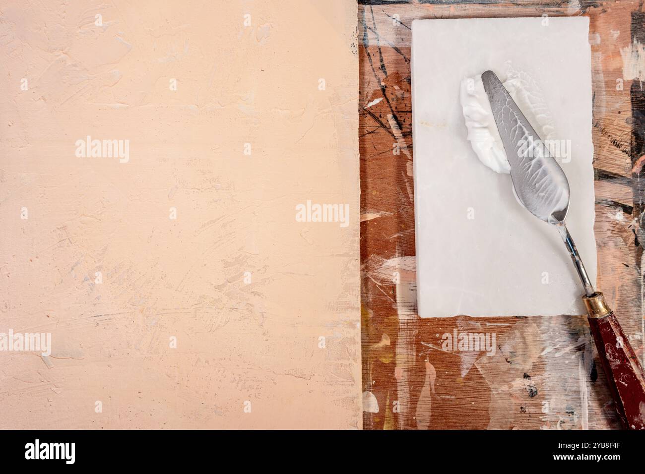 Von oben nach unten auf ein Palettenmesser mit Acrylfarbe und einer leeren, strukturierten Leinwand auf einem rustikalen Künstlerstudio in Großbritannien Stockfoto