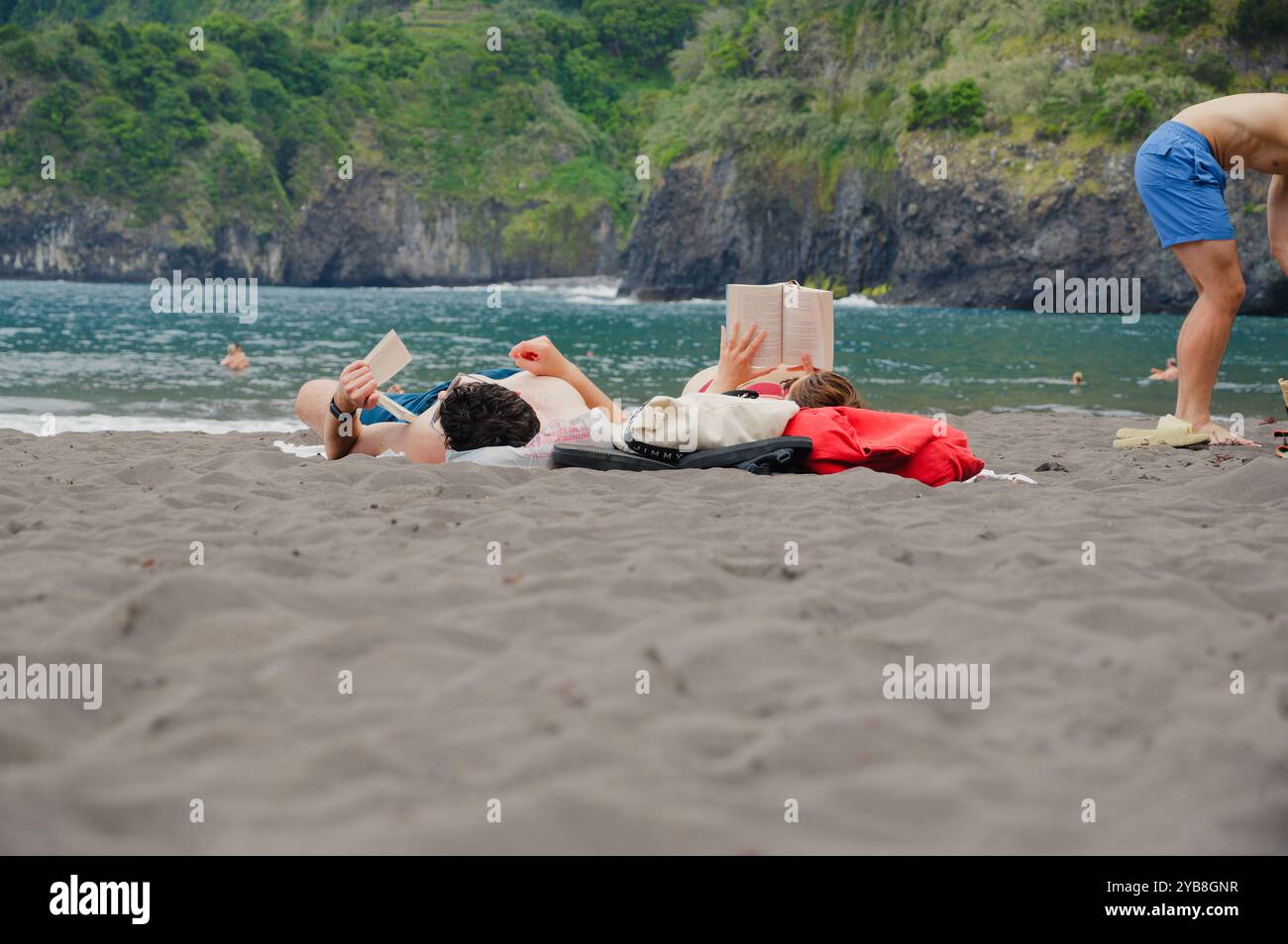 Ein Paar genießt einen entspannenden Tag am schwarzen Sand des Seixal Strandes mit üppigen Klippen und türkisfarbenem Wasser auf Madeira Stockfoto