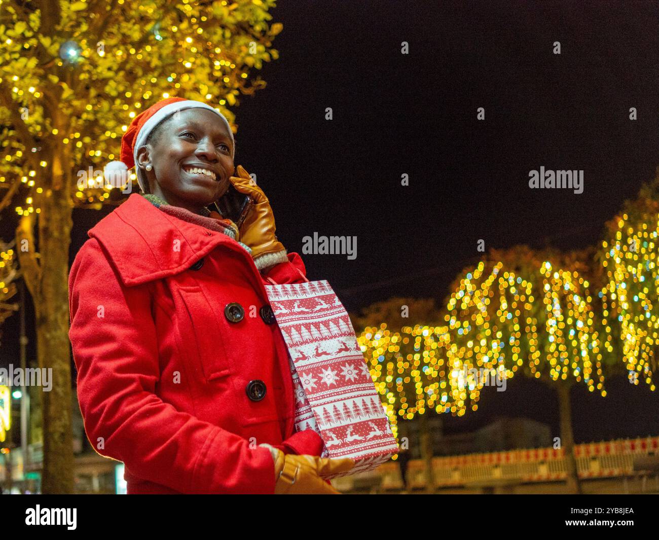Eine junge Frau, die ihr Handy während der Weihnachtszeit benutzt und einen Weihnachtsmann-Hut trägt Stockfoto