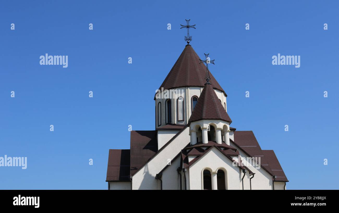 armenische apostolische Kirche, oberer Teil des hellen Gebäudes mit dunklem Dach und Kreuzen auf der Spitze, vor klarem blauem Himmel, christliche Architektur des kaukasus Stockfoto