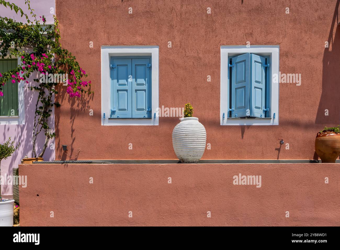 Ein bezauberndes Haus mit rosafarbenen Wänden in Assos, Kefalonia. Die hellblauen Fensterläden und die weißen Zierleisten bilden einen auffälligen Kontrast zur lebendigen Fassade. Rosa Stockfoto