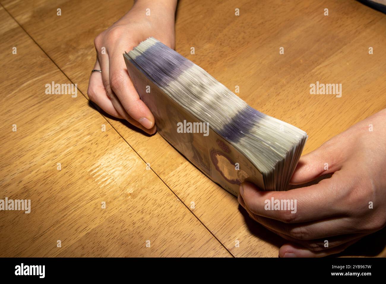 Eine Person, die einen dicken Stapel Bargeld auf einem Holztisch hält. Die Hände befinden sich auf beiden Seiten des Geldes und zeigen die Scheine. Die Ba Stockfoto