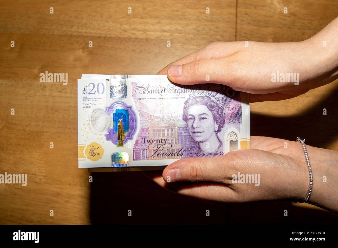 Eine Person, die eine britische Banknote im Wert von 20 £ mit dem Bild von Königin Elizabeth II. Hält. Die Banknote ist farbenfroh gestaltet und mit Sicherheitsmerkmalen versehen, die gegen einen gesetzt sind Stockfoto