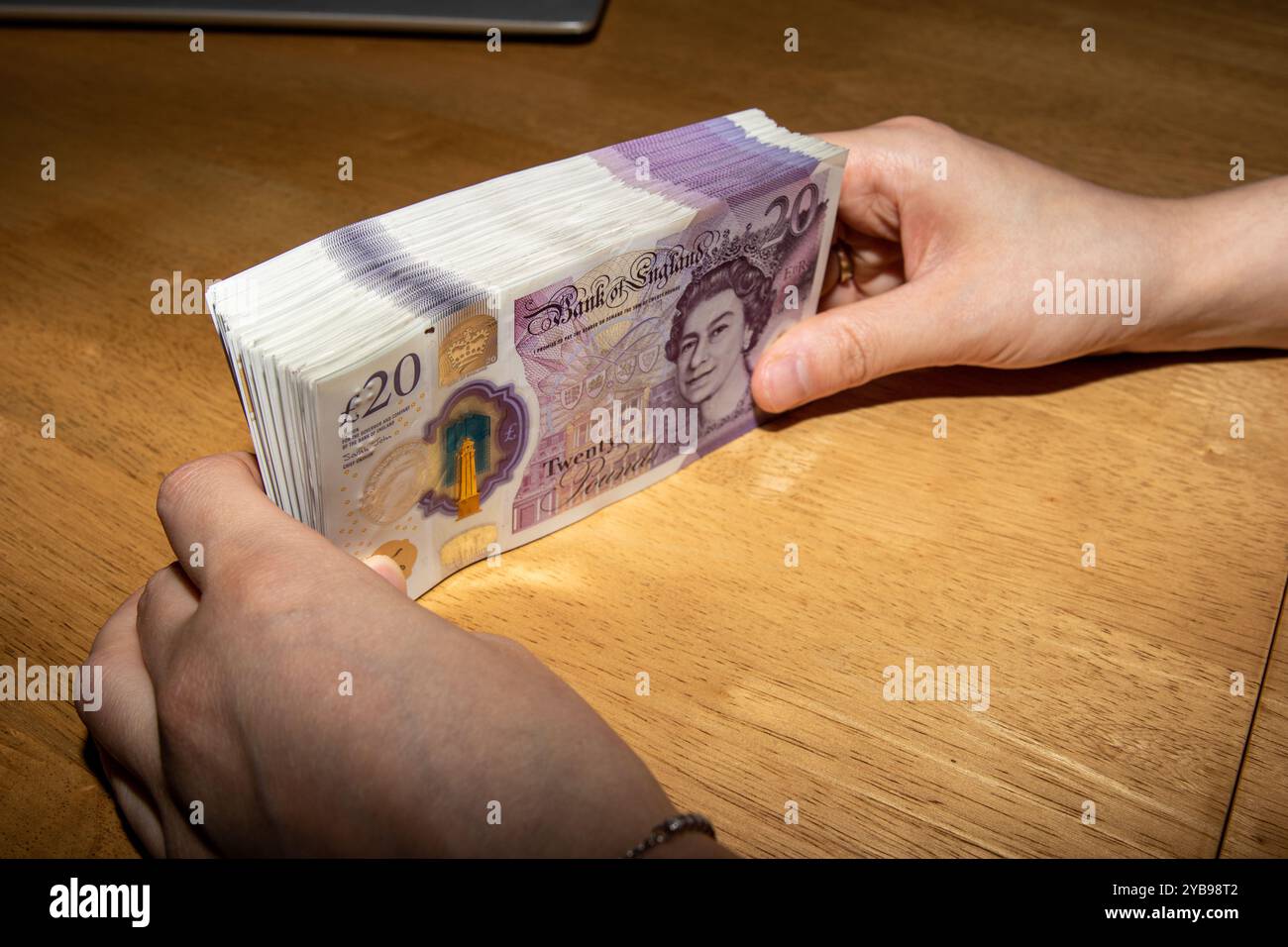 Eine Person, die einen Stapel britische Banknoten auf einem Holztisch hält. Die Noten sind ordentlich angeordnet und zeigen ihre violette Farbe und ihre Distink Stockfoto