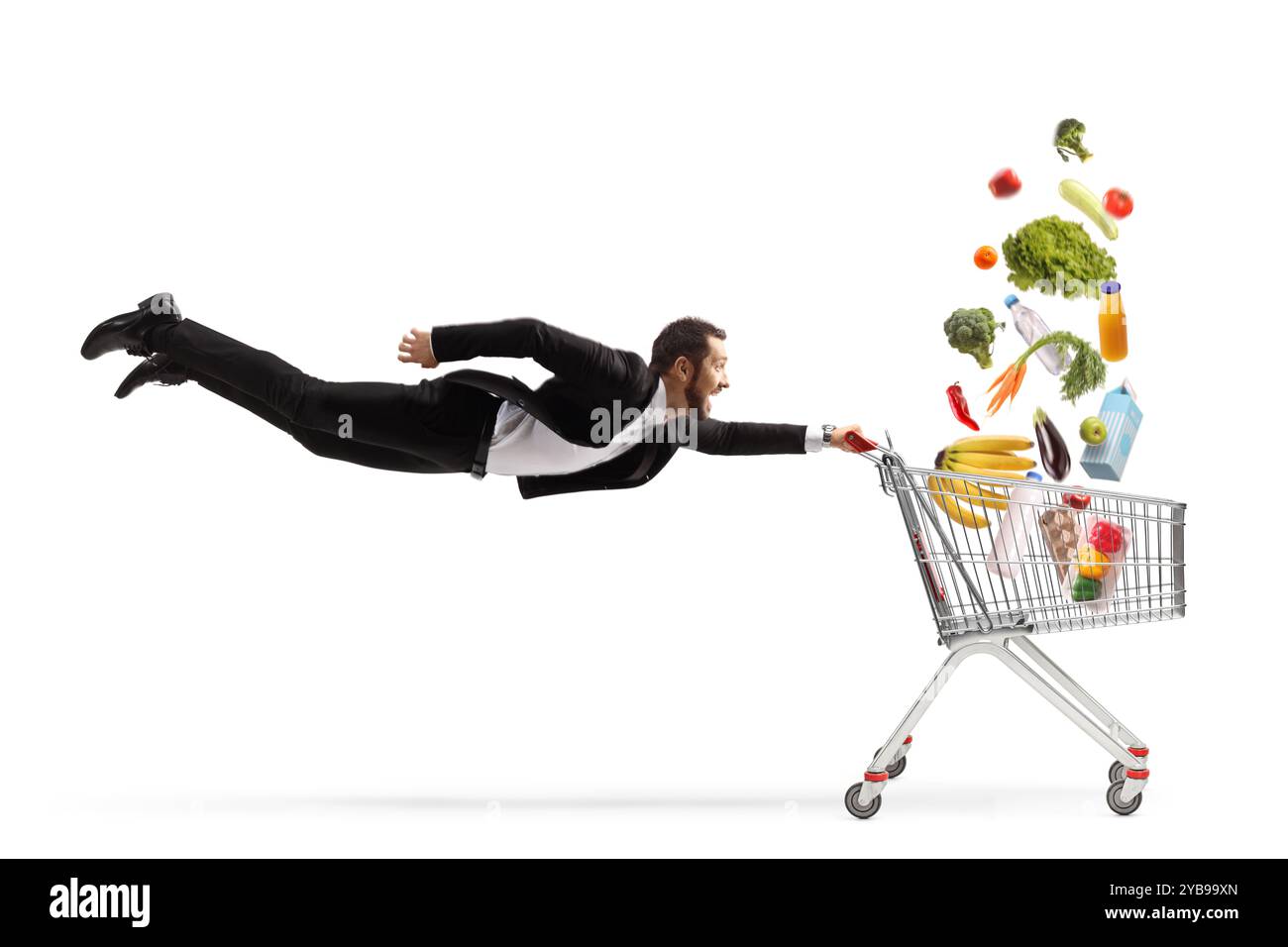 Aufnahme eines Geschäftsmannes in voller Länge, der einen Einkaufswagen mit fallenden Lebensmitteln auf weißem Hintergrund fliegt und hält Stockfoto