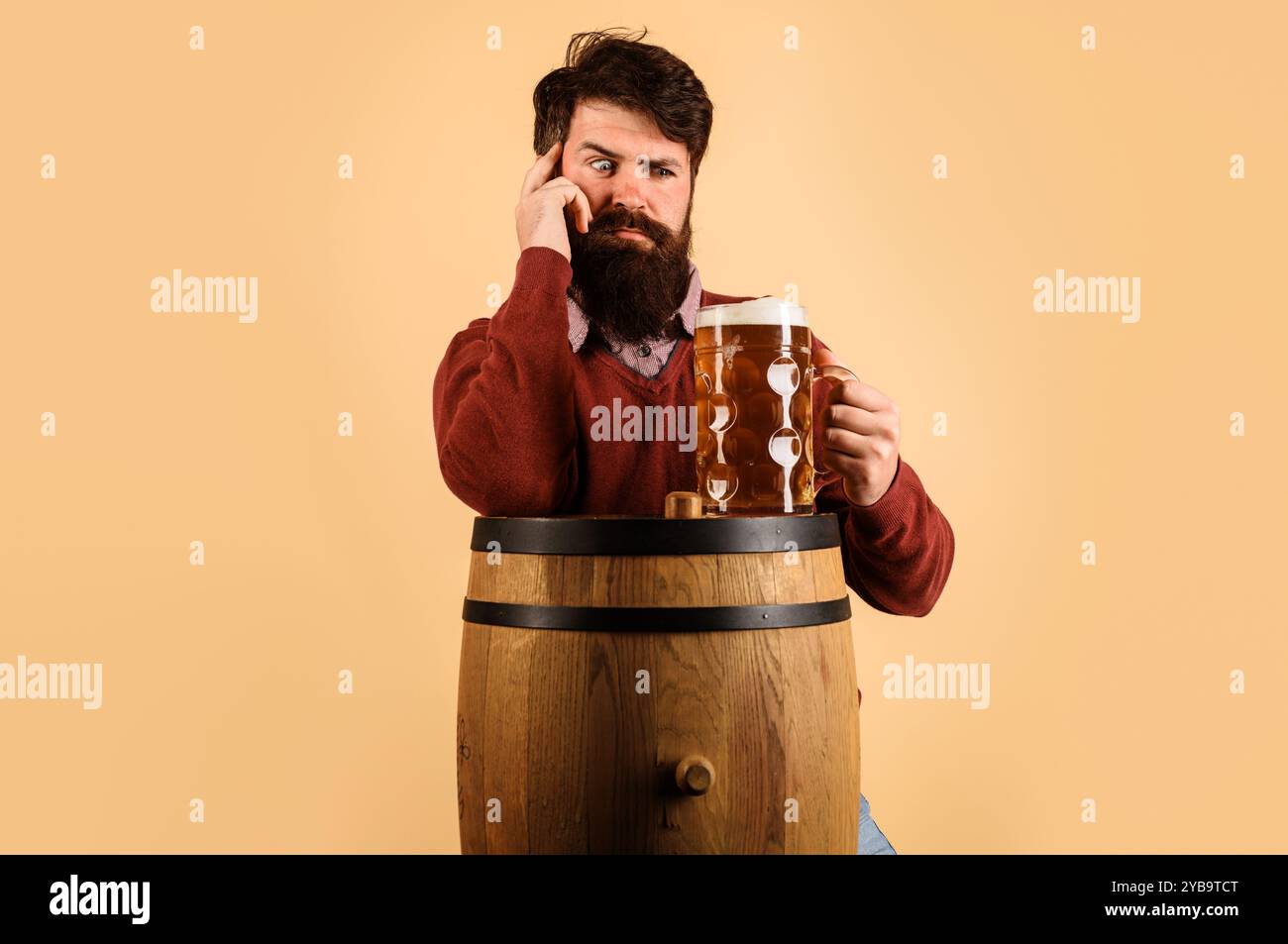 Bier für Pub, Bar oder Restaurant. Schöner Brauer mit einer Tasse köstlichem Craft-Bier auf Holzfässern. Bierzeit. Bärtiger Mann, der frisch gebrautes Bier probiert. Stockfoto