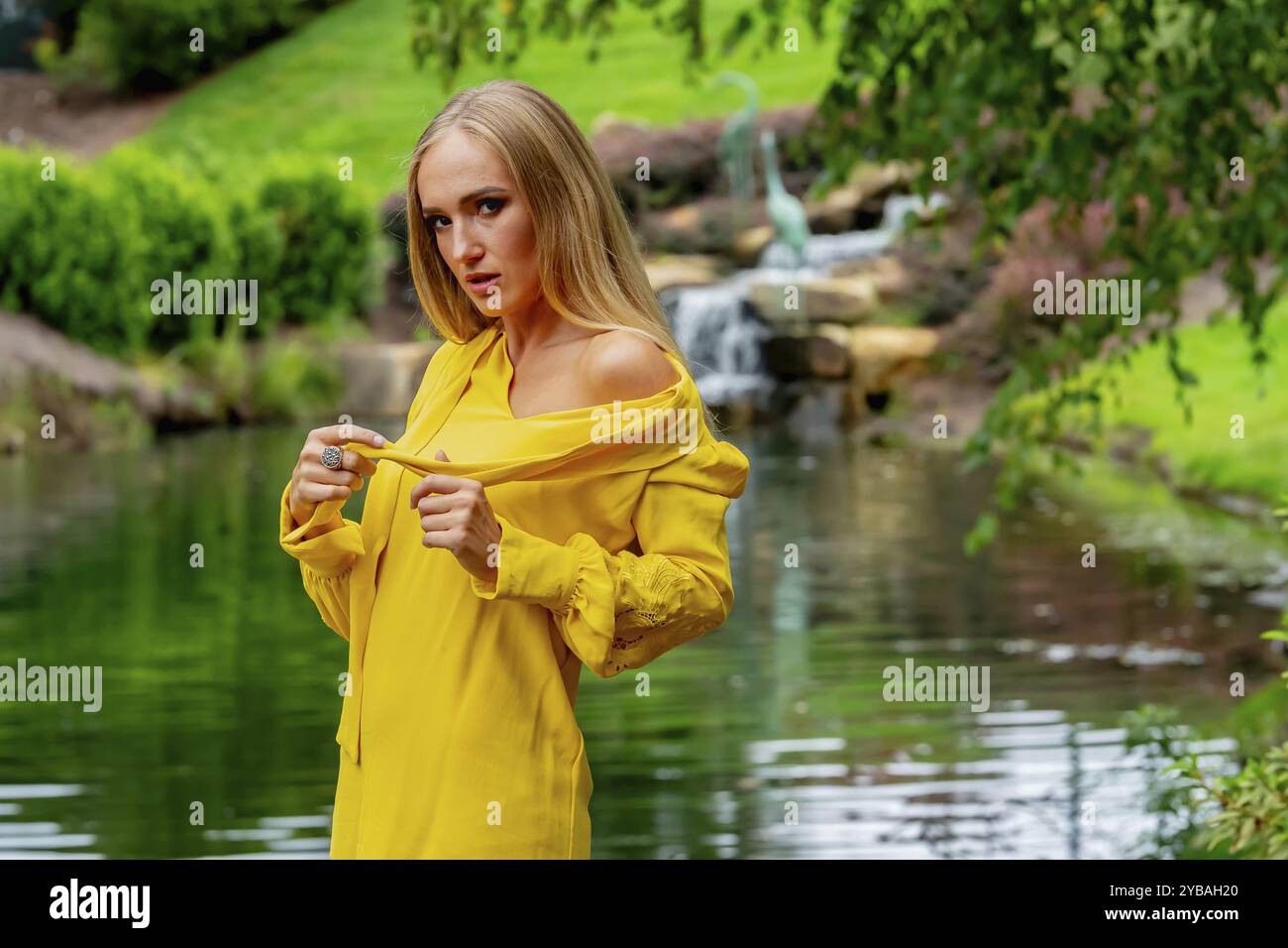 Blonde Schönheit erstrahlt in atemberaubender Herbstkleidung in der Nähe des Wasserfalls im Park, einer malerischen Herbstszene Stockfoto