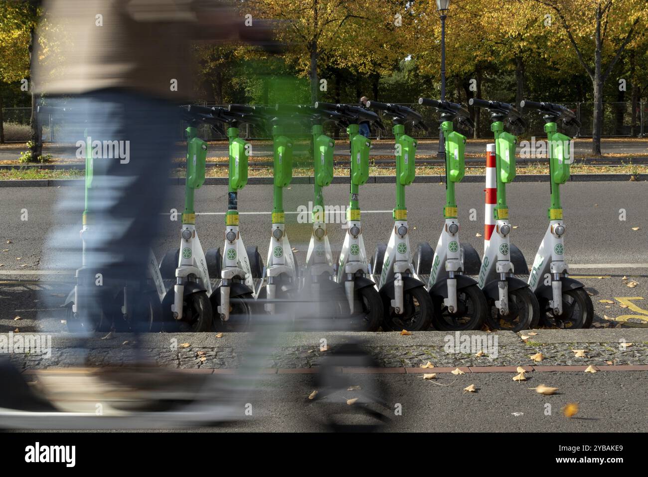 Verkehr, Mobilität, Bewegungsunschärfe, Rollerfahrer und aufgereihte E-Scooter des Anbieters Lime im Herbst auf einer Straße in Berlin, Deutschland, Europa Stockfoto