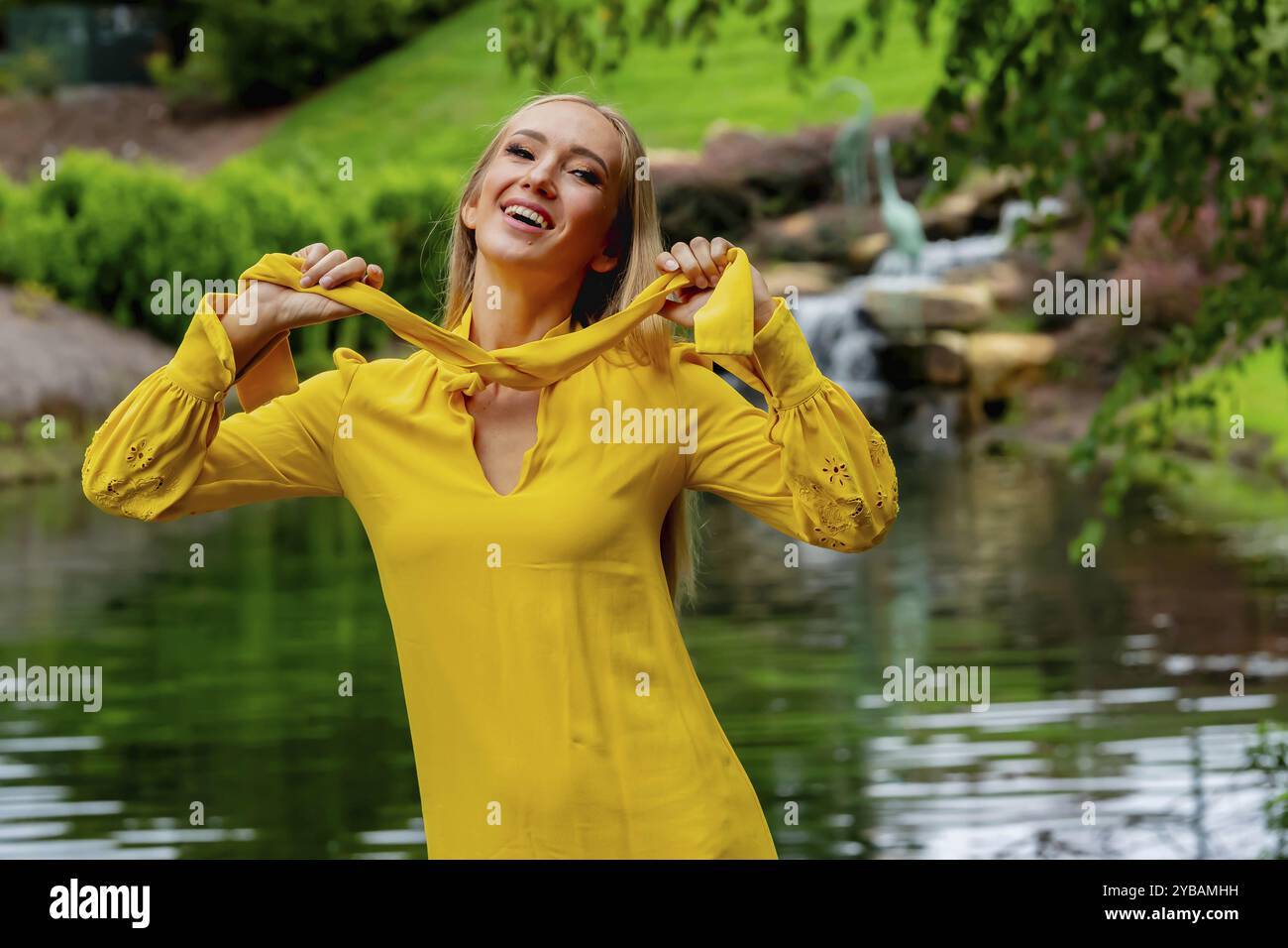 Blonde Schönheit erstrahlt in atemberaubender Herbstkleidung in der Nähe des Wasserfalls im Park, einer malerischen Herbstszene Stockfoto