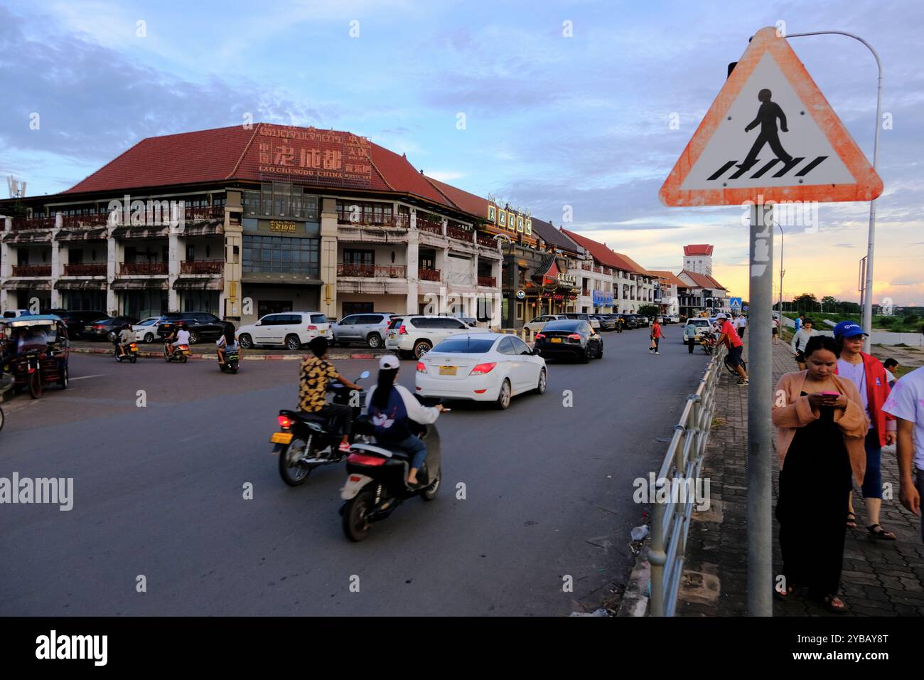 Verkehr auf der Sithane Road am Mekong River mit einem heruntergekommenen Einkaufs- und Restaurantkomplex im Hintergrund. Vientiane, Laos Stockfoto